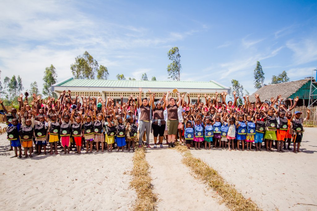 Viele Schulkinder sowie Lehrer und Lyreco-Mitarbeiter heben die Arme in die Luft und stehen vor einer Schule in Madagaskar.