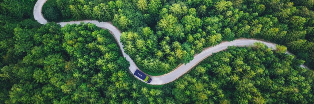 Aus der Vogelperspektive: Lyreco Auslieferfahrzeug fährt auf einer kurvigen Straße durch einen Wald.