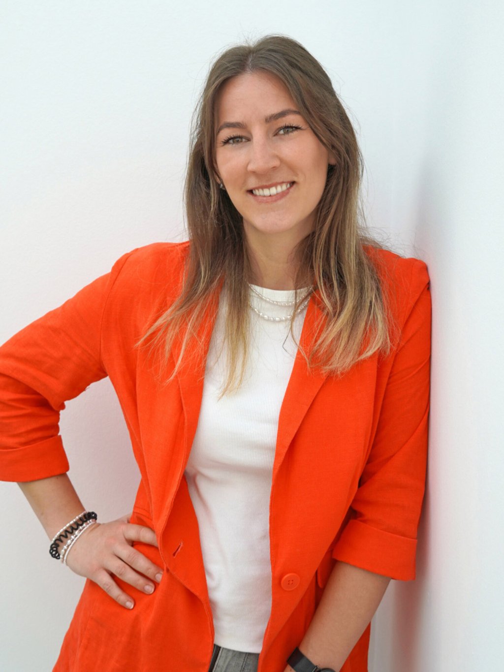 Junge Frau mit offenen Haaren und orangefarbenen Blazer, die in die Kamera lächelt. Nina Henze ist Recruiterin bei Lyreco Deutschland.