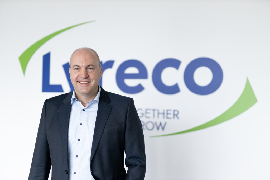 Geschäftsführer der Lyreco Deutschland GmbH, Frank Exslager, gekleidet in hellblauem Hemd und dunkelblauen Anzug steht lächelnd vor einer Wand, auf der das grün-blaue Logo von Lyreco ist.